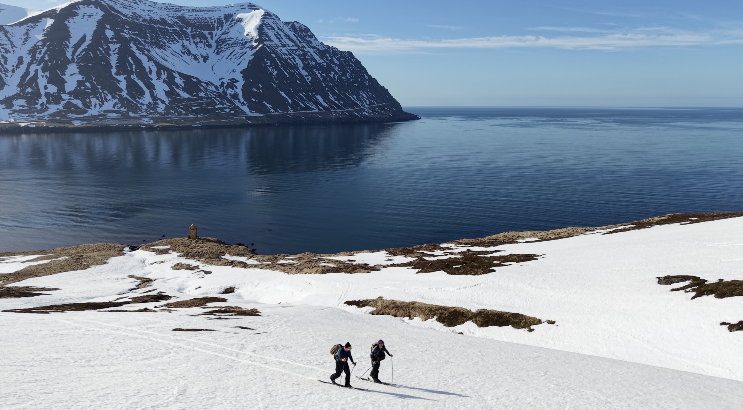 Zwei Skitourengeher über einem Fjord in Island